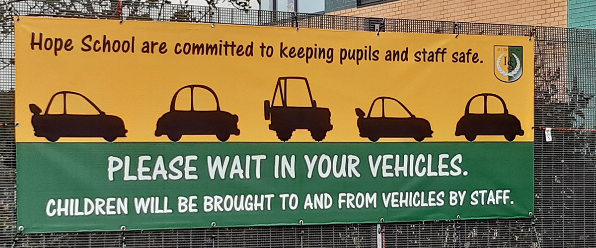 PVC banner giving drop off and collection information for parents at a Primary School during the Coronavirus Covid 19 times