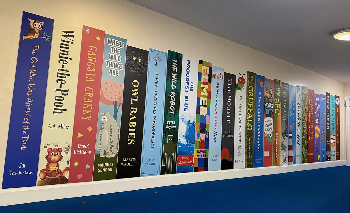 Book spine wall graphics on display in a school corridor featuring Primary age book titles