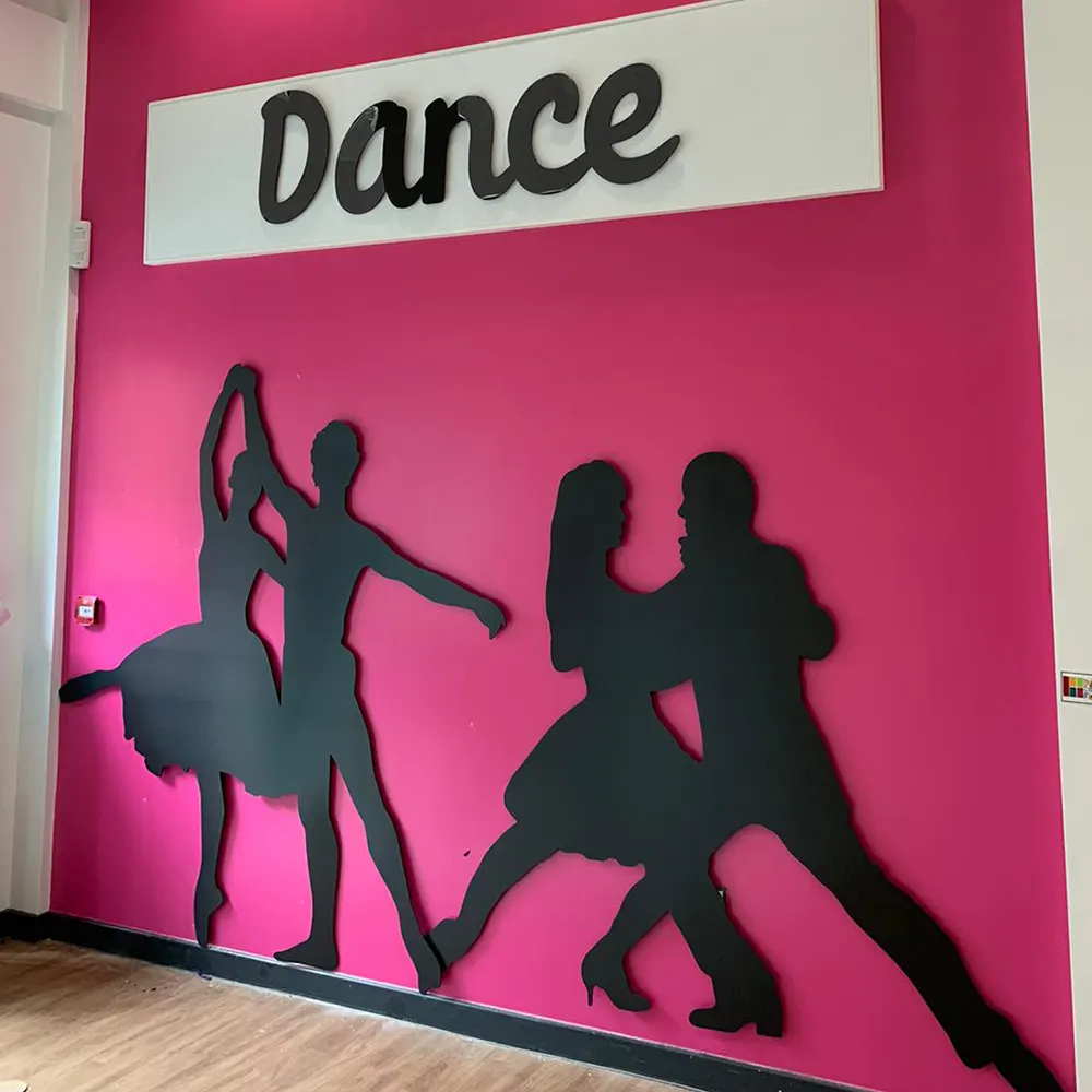 Bespoke black cut-out dance silhouette wall signs at Oxley Park Academy, Milton Keynes, featuring dancers fitted on a vibrant pink background.