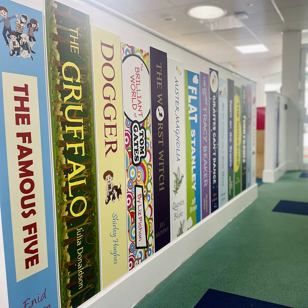 Book spine wall graphics in the corridor at Trenance Learning Academy, Newquay, featuring popular primary school book titles.