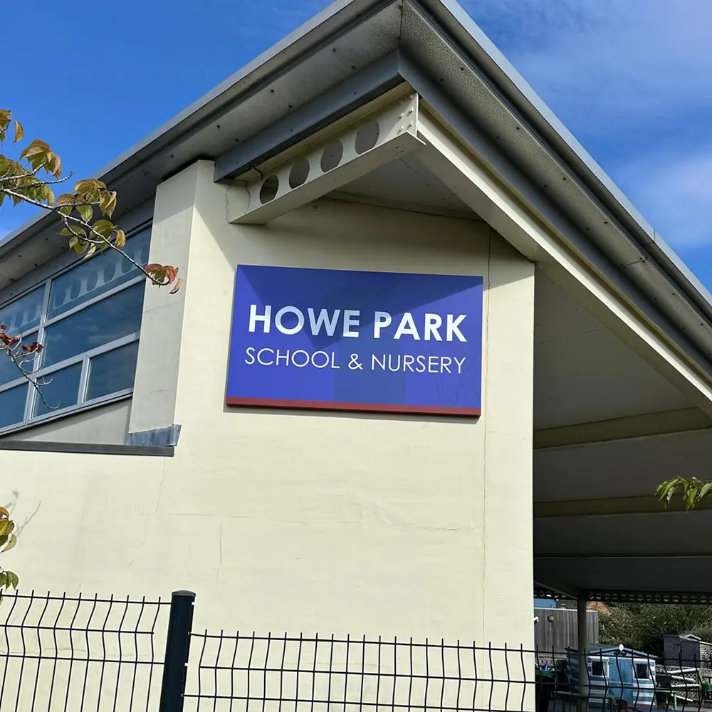 Main school entrance sign showing school name with the school woodpecker logo faded into the background - Howe Park School, Milton Keynes